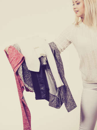 Woman holding pile of winter clothes, can not decide what to wear. Picking winter clothing concept.の写真素材