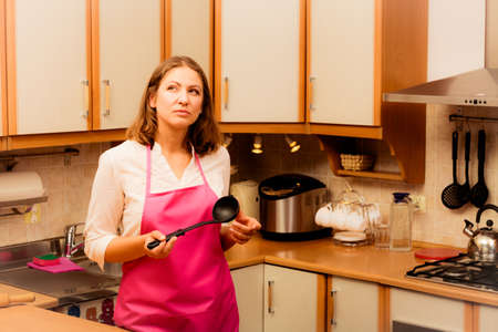 Cooking and preparing food meal concept. Thoughtful wondering and dreaming woman chef cook housewife holding ladle spoon in kitchen.の写真素材