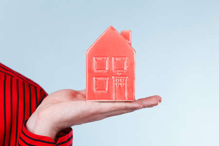 First flat apartment. Step forward concept. Male hand holding little small red house home. Part body man with idea of growing up.の写真素材