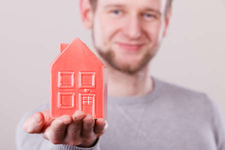 Symbolism housing safety family finances mortgage concept. Young man holding house on palm. Male presenting home model.の写真素材