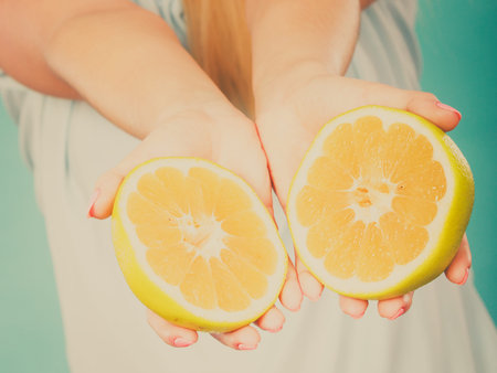 Halfs of yellow grapefruit citrus fruit in female hands closeup. Woman dietician recommend healthy diet nutrition.の写真素材