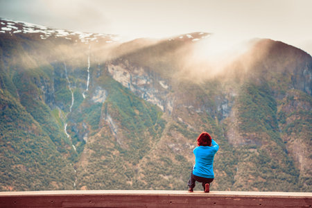 Tourism and travel. Woman tourist taking photo with camera, enjoying mountains fjords view in Sogn...