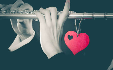 Valentines day love melody concept. Flute music playing man flutist musician performer. Male hands with instrument and red heart, close upの写真素材