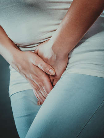 Closeup young sick woman with hands holding pressing her crotch lower abdomen. Medical or gynecological problems, healthcare conceptの写真素材