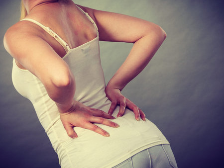 Long working hours and health. Young female with backache. Woman suffering from back pain on gray