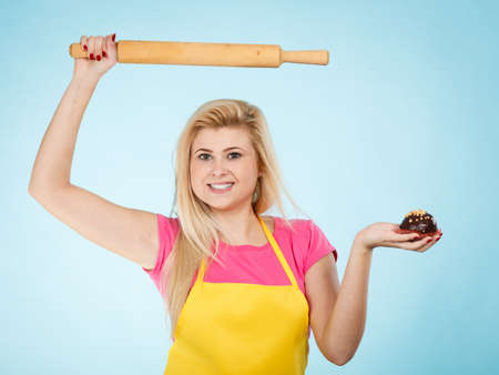 Baking tasty desserts sweets at home concept. Woman holding delicious chocolate cupcake and rolling pin wearing yellow apron.の写真素材