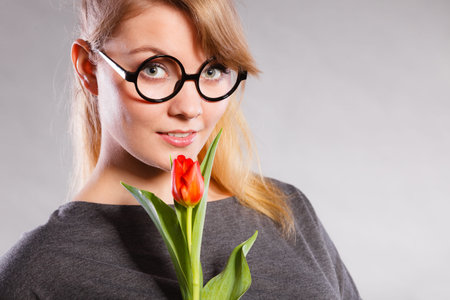 Delicacy and subtlety of women. Young adorable woman with spring flower. Portrait of beauty delicate girl in glasses with red beautiful tulip.の写真素材