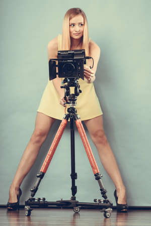 Photographer girl shooting images. Attractive fashionable blonde woman in full length taking photos with camera on blueの写真素材