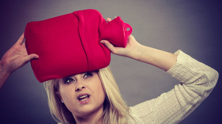 Woman holding red hot water bottle on head to deal with headache