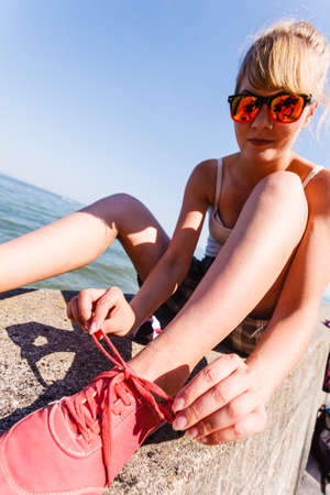 Outdoor relax holidays nature concept. Young girl tying shoelace. Lady sunbathing on coast making a knot.の写真素材