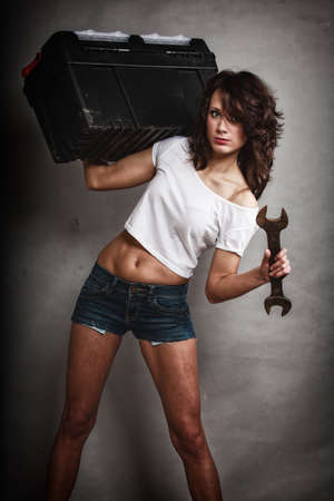 Sex equality and feminism. Sexy girl holding toolbox and wrench spanner on gray. Young attractive woman working as construction worker. Studio shot.の写真素材
