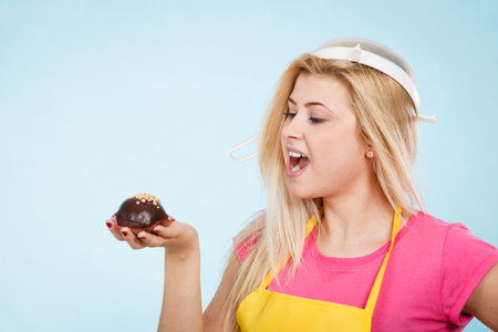 Baking tasty desserts sweets at home concept. Woman holding delicious sweet chocolate cupcake wearing apron and colander on head as hat.の写真素材