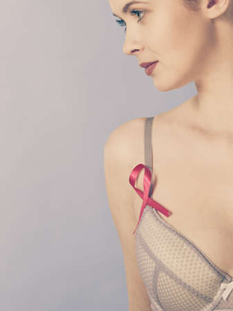 Health care, medicine and breast cancer awareness concept. Young woman in bra with pink ribbon symbol against blueの写真素材