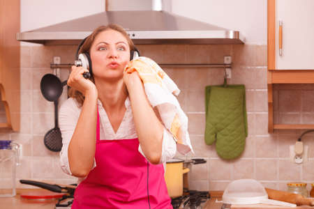 Cooking preparing and making food concept. Modern beauty woman housewife cook chef wearing pink apron and listening music on earphones standing in kitchen.の写真素材