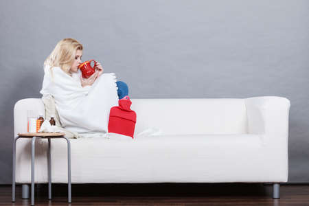 Sickness, seasonal virus problem concept. Woman being sick having flu lying on sofa holding mug cup with hot drink.の写真素材