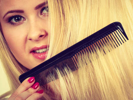 Hair care, hair styling concept. Blonde woman brushing her long hair with black comb.の写真素材