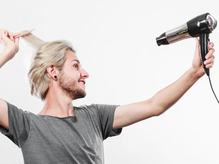 Hairstyle and fashion. Young trendy male hairstylist barber with new idea of look changing. Blonde man holding hair dryer and comb creating new hairdoの写真素材