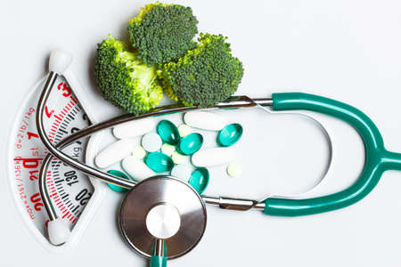 Diet healthy eating weight control and health care concept. Closeup green broccoli stethoscope pills on white scales, choice betweenの写真素材