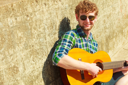 Music and people concept. Young bearded hipster man with guitar outdoor on street