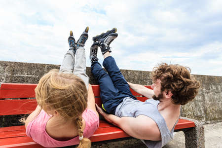 Young tired people friends in training suit with roller skates. Woman and man relaxing lying on bench outdoor.の写真素材