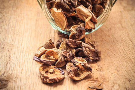 Food. Closeup dry mushrooms spilling out from storage jar on wooden surface table background.の写真素材