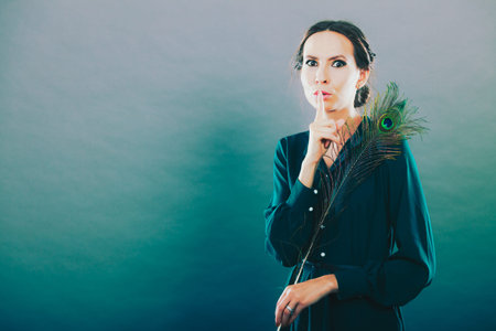portrait of beautiful woman holding peacock feather finger on lips silence hand gesture