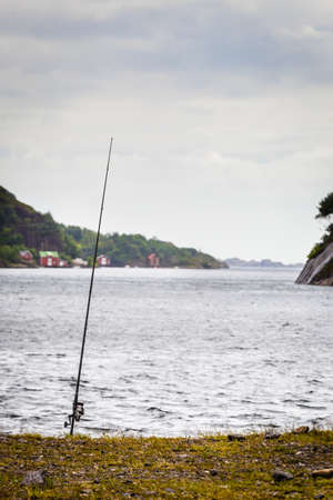 Fishing rod left alone on shore near lake and mountains. Cloudy scandinavian weather.の写真素材