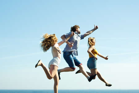 Carefree young friends people jumping outdoor on sky background. Happy women and man having fun. Summer happiness and freedom.の写真素材