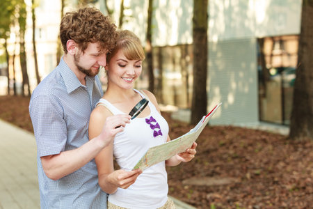 Summer travel concept. Young tourist couple on vacation in city looking up directions on map holding magnifying glassの写真素材