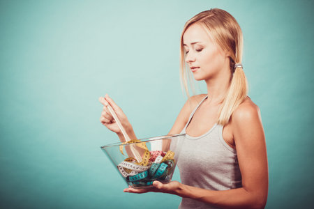 Diet, healthy eating, weight loss and slim body concept. Fit fitness girl holding bowl with many colorful measuring tapes studio shot on blue copy spaceの写真素材