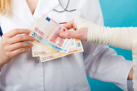 Corruption in healthcare industry. Female doctor bandaging male hand. Man giving money to woman. Bribery in medicine.の写真素材