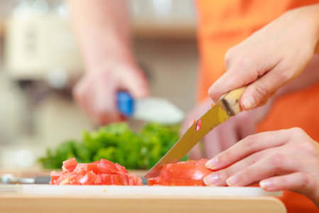 Healthy eating, vegetarian food, cooking, dieting and people concept. Couple in kitchen at home preparing fresh salad slicing vegetables on cutting boardの写真素材