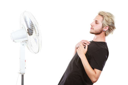 Air conditioning, heat, artistic concept. Young man in front of cooling fan, artistic way fighting with wind, studio shot isolated.の写真素材