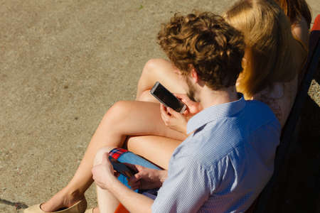Friends texting using mobile phones outdoor. Young women and man browsing internet on smartphone. Summer relax.の写真素材