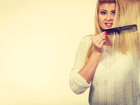 Hair care, hair styling concept. Blonde woman brushing her long hair with black comb.の写真素材