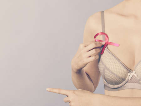 Health care, medicine and breast cancer awareness concept. Woman in bra with pink ribbon symbol pointing with finger to copy space, on blueの写真素材