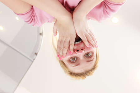 Shocked woman with hands on face standing in bathroom. Shock, amazed face expressions concept. View from bottomの写真素材