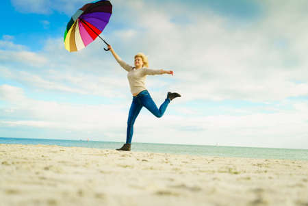 Happiness, enjoying weather, feeling great concept. Woman jumping with colorful umbrella on beach near sea, sunny day and clear blue skyの写真素材