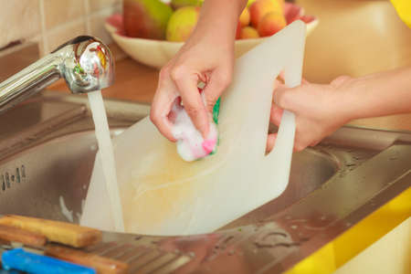 Household. Closeup woman doing the washing up in kitchen cleaning plastic cutting boardの写真素材