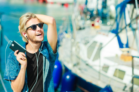 Vacation, relaxation, passion concept. Young fashionable blonde in sunglasses man relaxing, listening to music and enjoying beautiful, sunny weather. Outdoor shotの写真素材