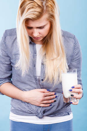 Lactose intolerance, health problem with dairy food products concept. Woman holding glass of milk having bad stomach ache.の写真素材