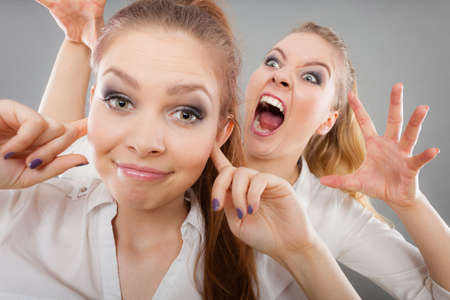 Conflict, bad relationships, friendship difficulties. Two young women having argument. Angry fury girl screaming at her friend or younger sister, female closing his ears, not listeningの写真素材