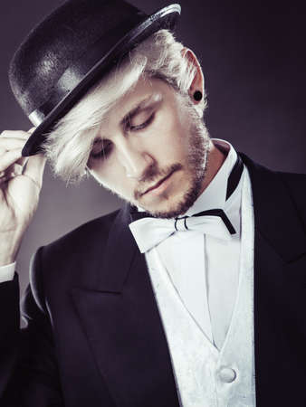Tuxedo, male fashion, classical look concept. Elegantly dressed man wearing black fedora hat. Studio shot on dark backgroundの写真素材
