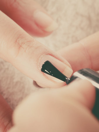 Closeup of beautician painting nails of female client. Woman in beauty spa salon doing manicure