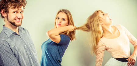 Aggressive mad women fighting over man pulling hair. Young jealous girls wooing guy. Violence.の写真素材