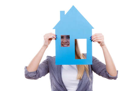 Dream about stabilization and family. Blonde girl holding blue paper house model cutout. New flat apartment. Isolated on whiteの写真素材