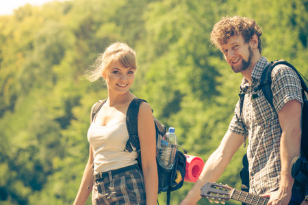 Adventure, tourism, enjoying summer time together - Hiking young couple with guitar backpack...