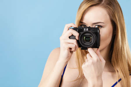 Young woman holding old fashioned analog camera taking pictures. Studio shot on blue background.の写真素材
