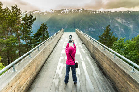 Tourism and travel. Woman tourist nature photographer taking photo with camera, enjoying Aurland fjord landscape from Stegastein lookout, Norway Scandinavia.の写真素材
