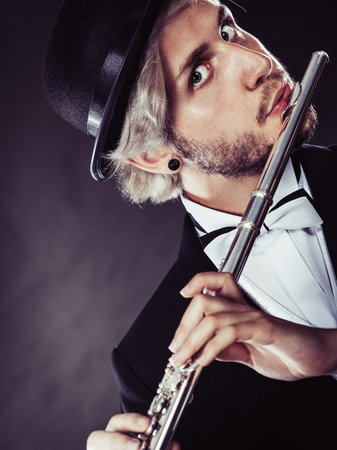 Classical music, passion and hobby concept. Elegantly dressed musician man playing on flute wearing black fedora hat. Studio shot on dark grey backgroundの写真素材